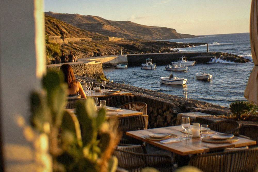 A seafront terrace with tables set for dinner beside a harbour wall