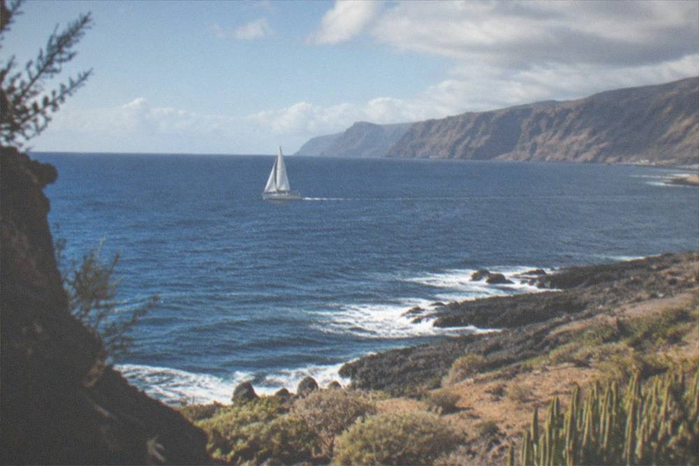 A sailboat under way on open water with cliffs visible in the distance