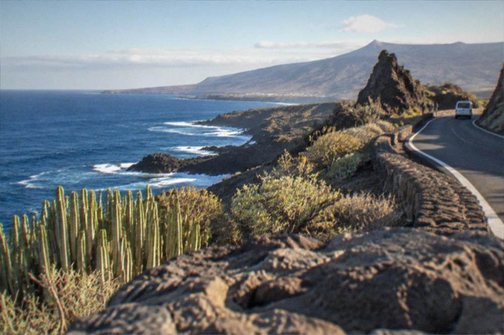 A volcanic mountain road rising above cloud level with rock formations at the roadside