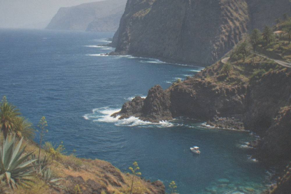 A small boat anchored in a rocky cove with clear water below tall cliffs