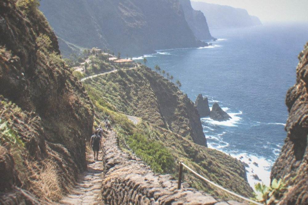A narrow rocky gorge path with steep rock walls leading down towards the sea