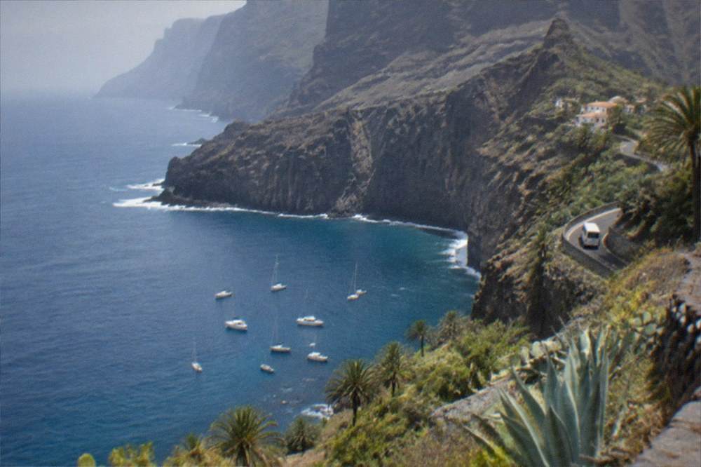 A calm blue bay with dark cliffs and small boats anchored in clear water