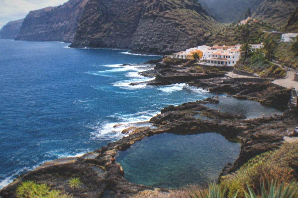 Rock pools of dark volcanic stone filled with sea water beside a small coastal town