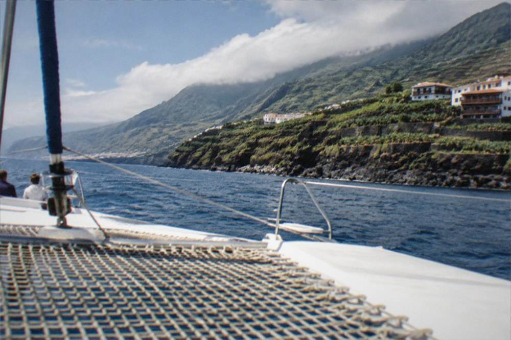 Catamaran on open water with dark volcanic coastline in the distance