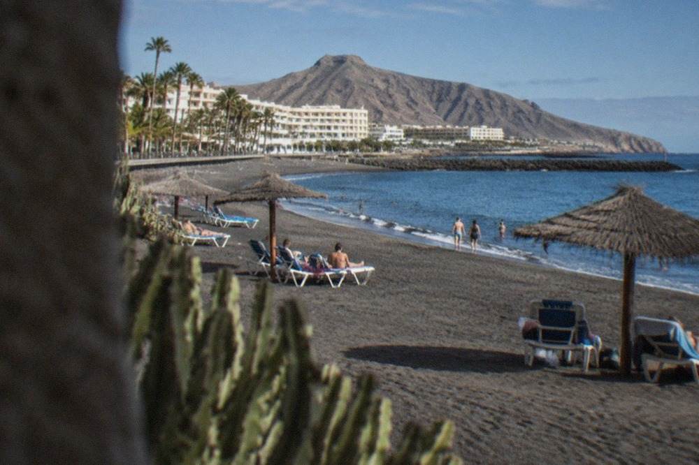 A wide sandy beach in a Tenerife resort with sun loungers, parasols and calm blue water