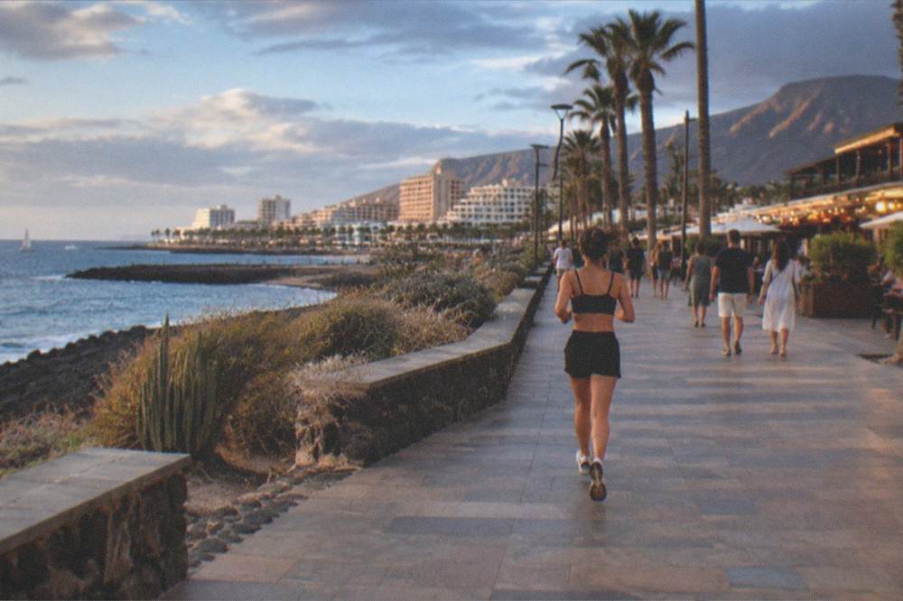 A busy evening promenade with lit bars and restaurants and people walking under palm trees