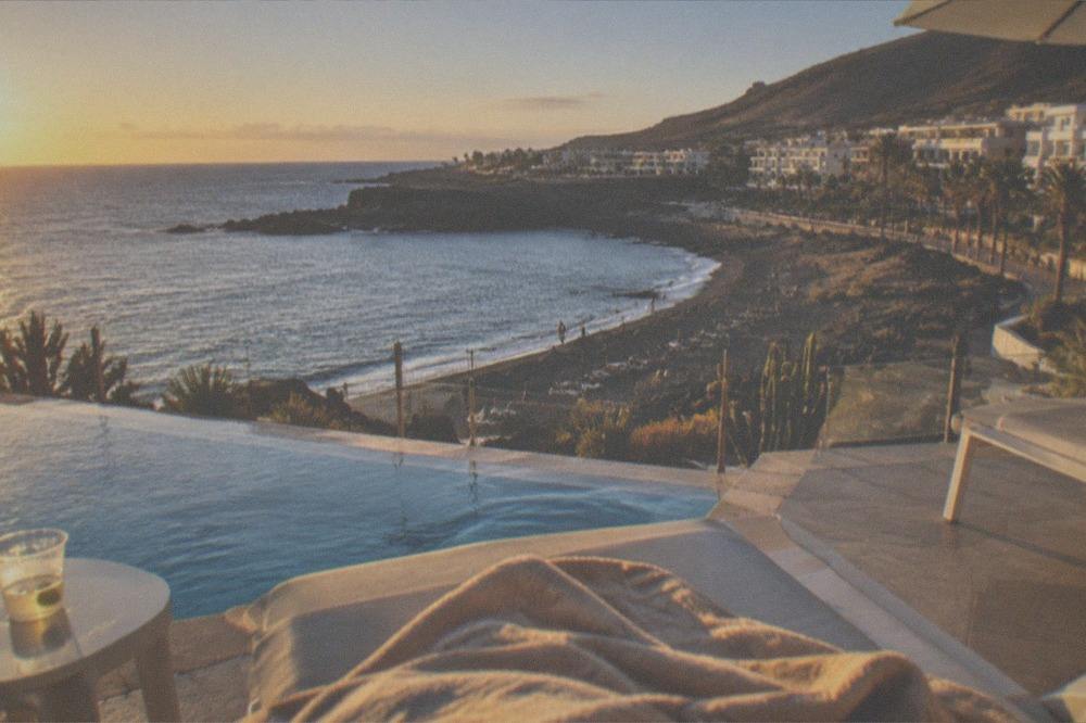 Hotel terraces and a pool overlooking a small bay with sun umbrellas on the sand