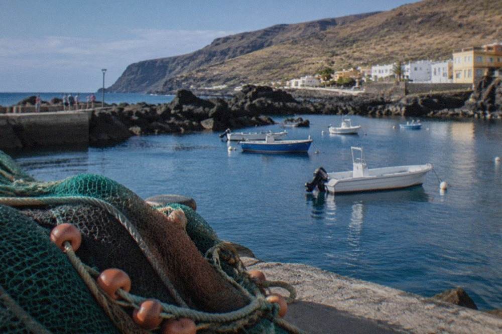 A small harbour town on Tenerife's west coast with calm water and dark volcanic rock along the shore