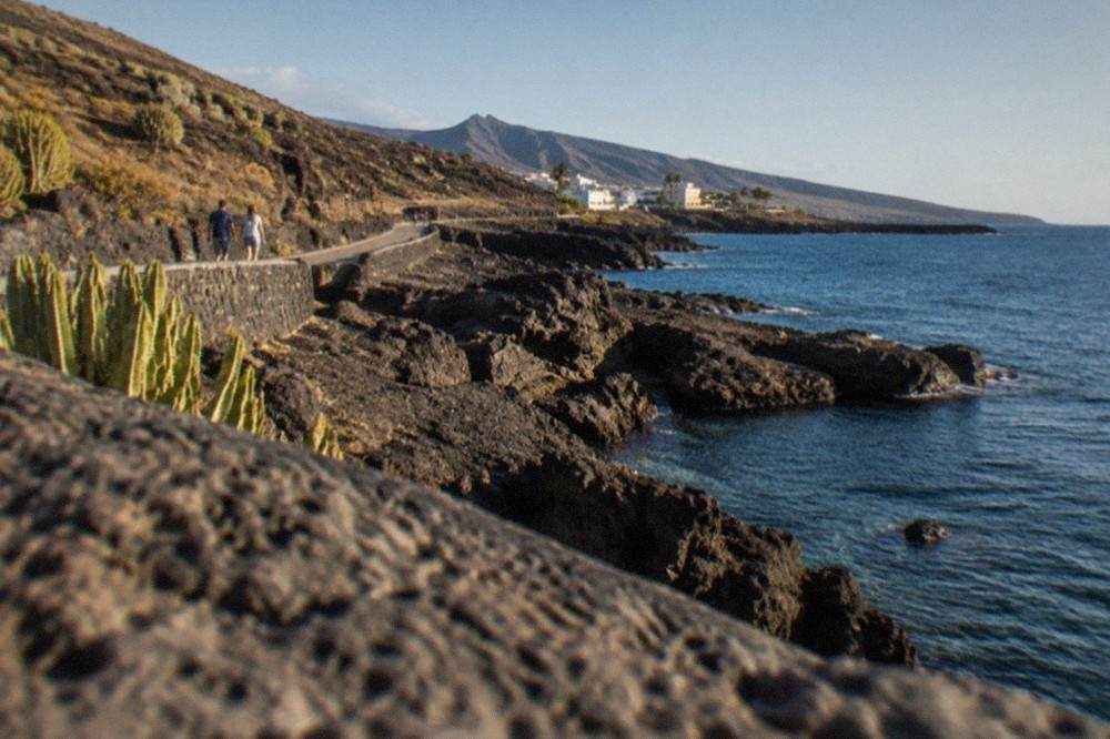 Dark volcanic rocks and clear blue water along a quiet coastal road in southwest Tenerife
