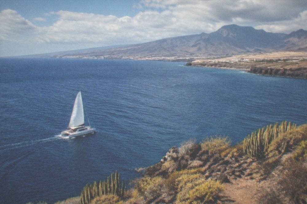 A catamaran under sail on open water with the Tenerife coastline in the distance