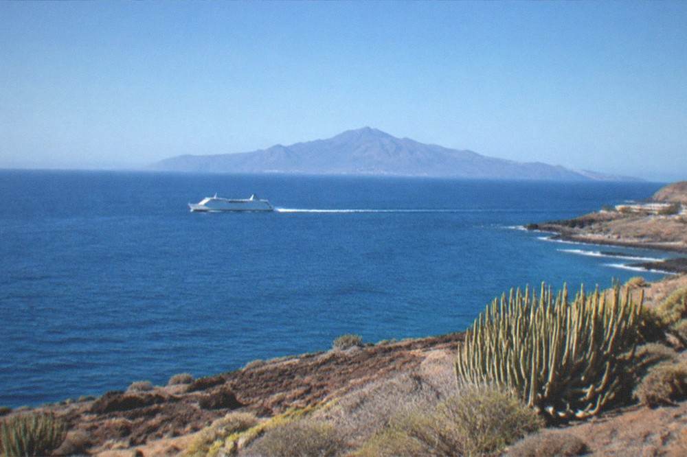 A ferry at sea with a volcanic island on the horizon under a clear sky