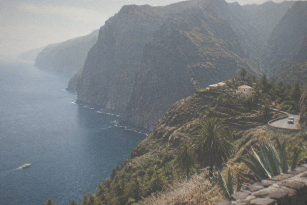 Tall dark sea cliffs rising above calm water with a small boat below