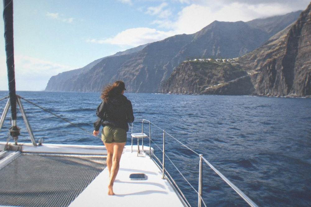 A catamaran on open water with dark cliffs in the distance