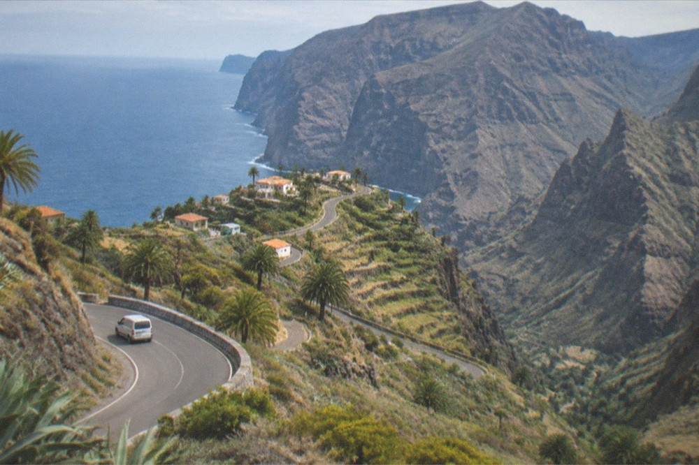 A winding mountain road in Tenerife with terraced hillsides and the sea in the distance