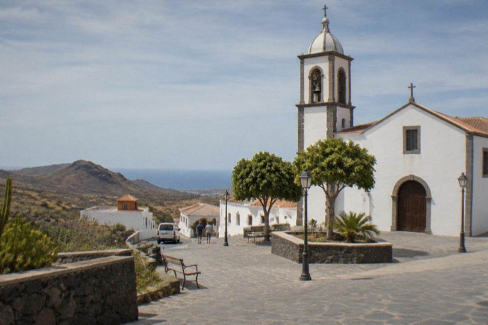 White-walled Canarian buildings and a church tower above a small town square