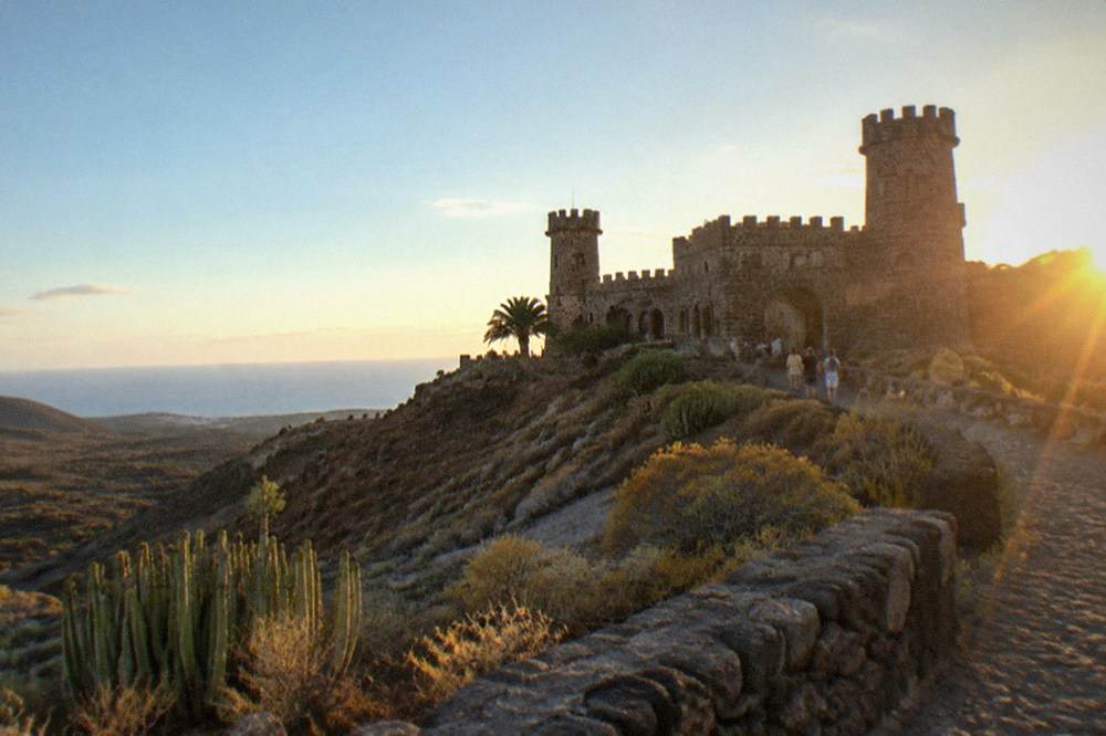 A stone castle-style building with towers lit in the early evening