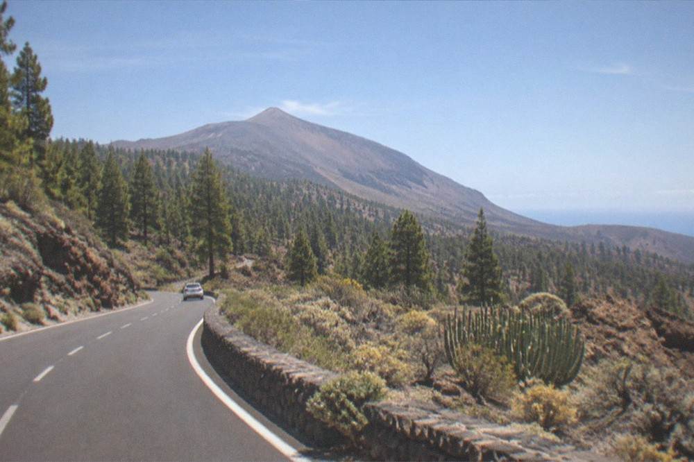 A volcanic mountain road rising through pine forest towards a bare summit