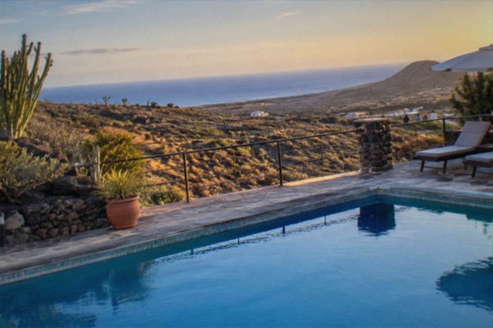 A calm swimming pool and terrace in evening light with the sea in the distance