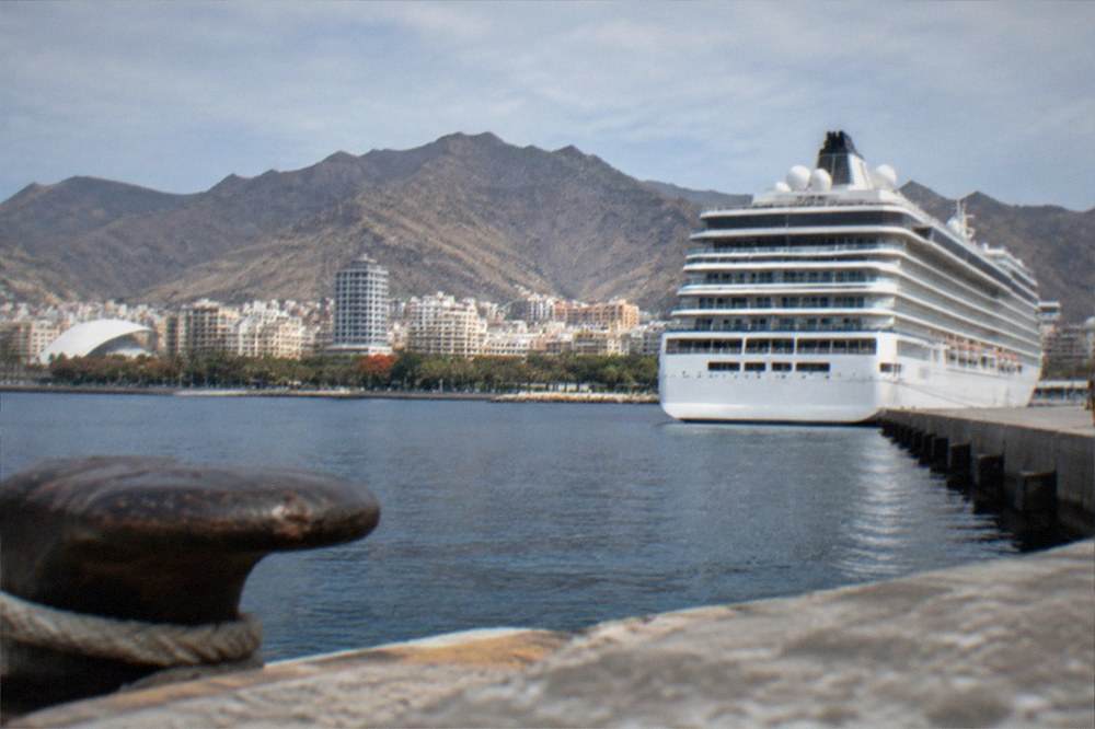 Cruise ship docked at a port with a city skyline behind it
