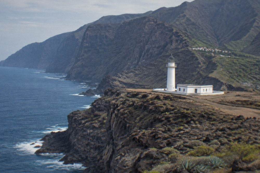 White lighthouse on the flat lava headland of Punta de Teno with cliffs behind