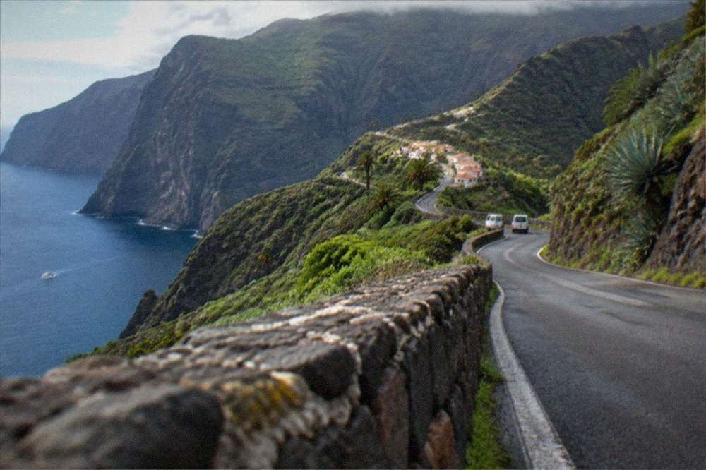 Narrow mountain road winding through green ridges toward the village of Masca