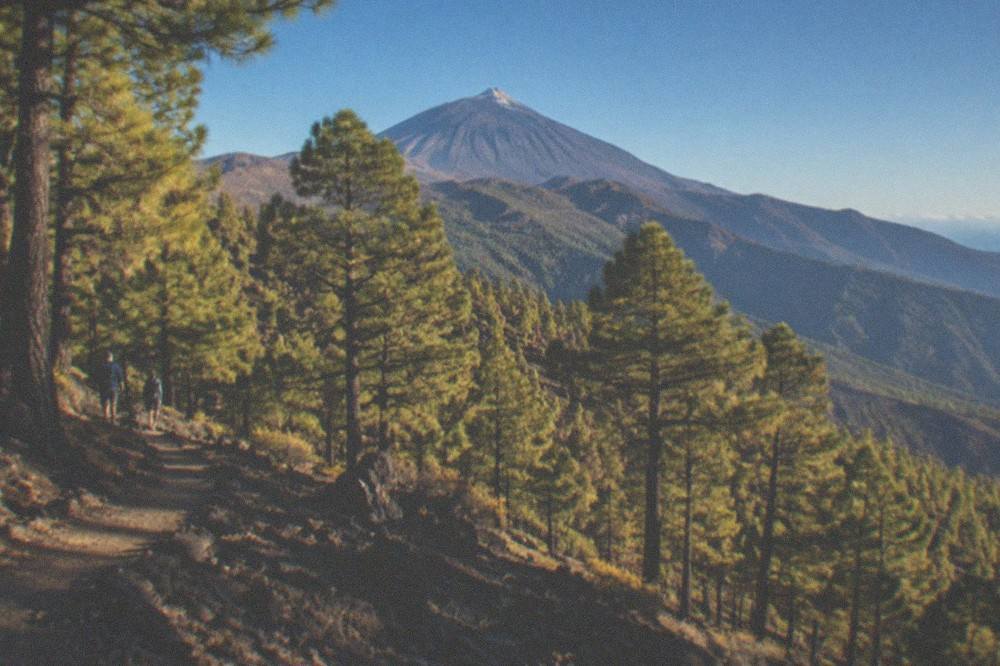 A panoramic view of a volcanic peak rising above layered mountain slopes under a deep blue sky