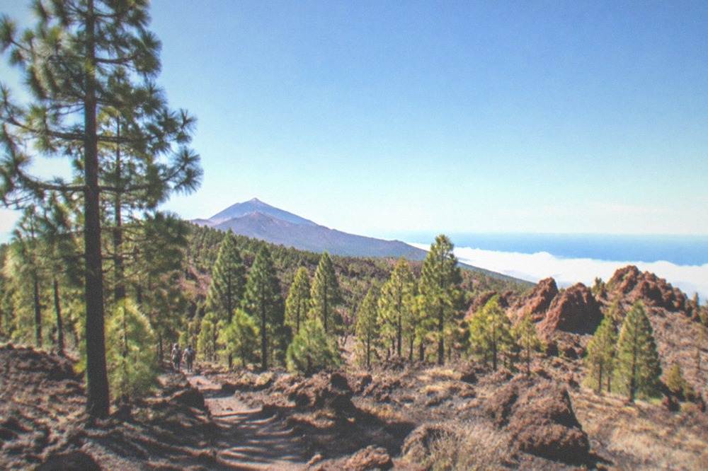 A high volcanic plateau with reddish rock formations and a clear sky above the clouds