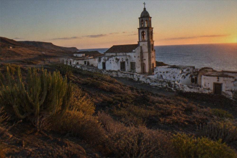 The tower of an empty church rising above abandoned white buildings at dusk