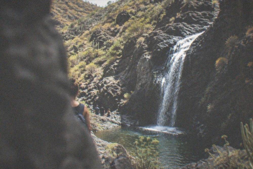 Water falling over dark rock into a small pool at the head of a ravine