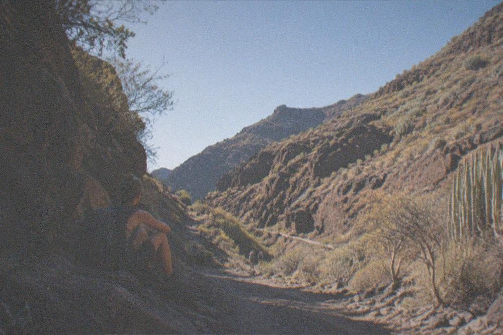 A hiker with a backpack resting at a shaded bend in a rocky gorge path