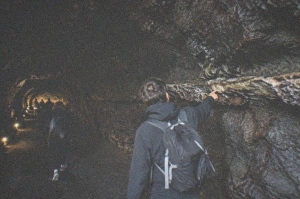 A guide pointing at a lava ledge on the wall of a dimly lit cave passage