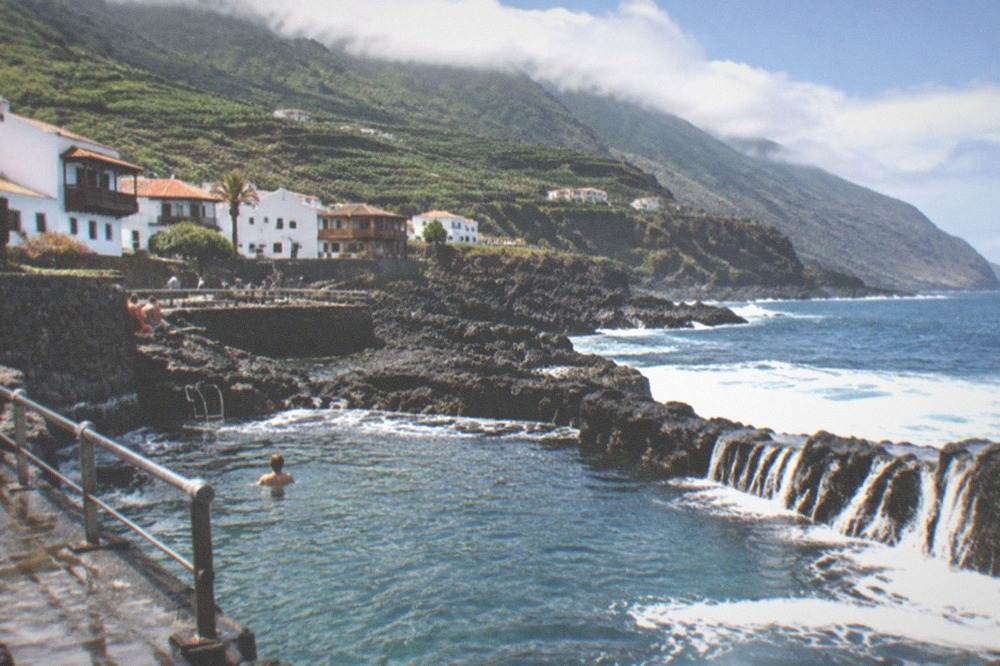 Sea water spilling over dark rock into a natural pool with white foam at the edge