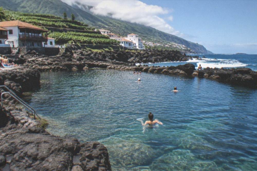 People swimming in a large natural rock pool with dark volcanic walls and clear water