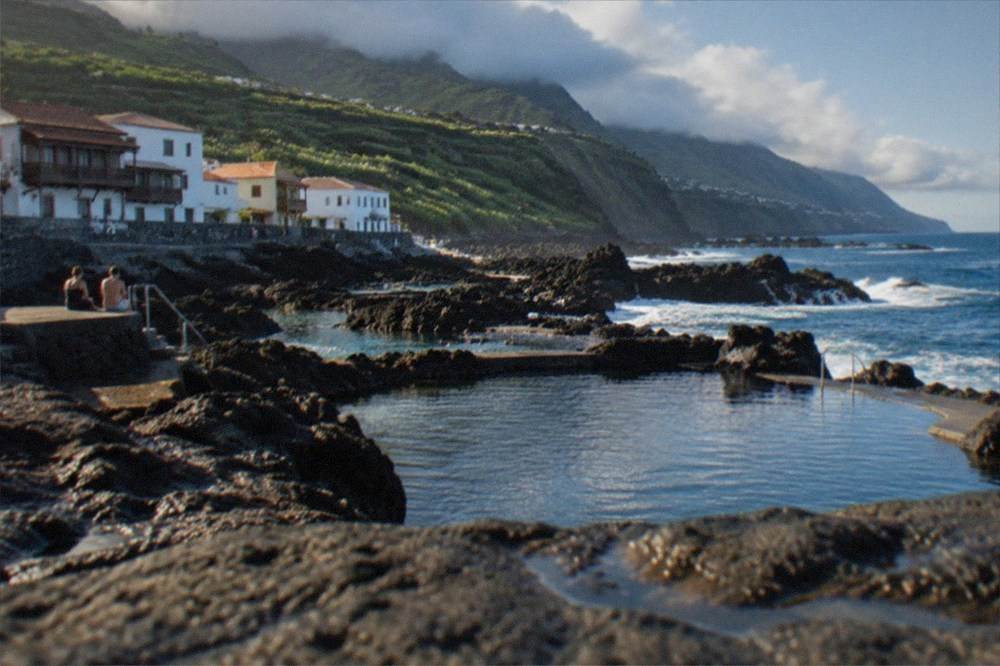 The coastline of northern Tenerife with dark rock, green slopes and the sea under a bright sky