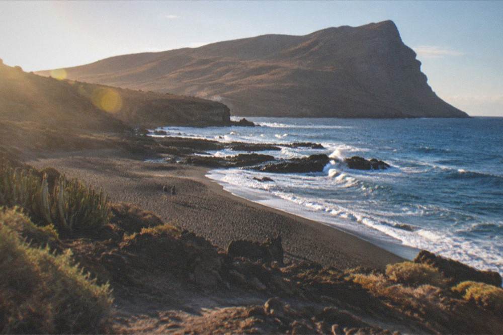 Dark volcanic sand in a rocky cove with Atlantic waves breaking white