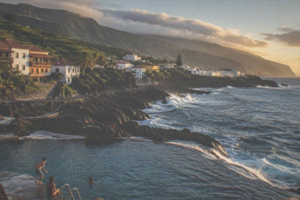 Children playing at the edge of a lido pool with volcanic rock and sea beyond
