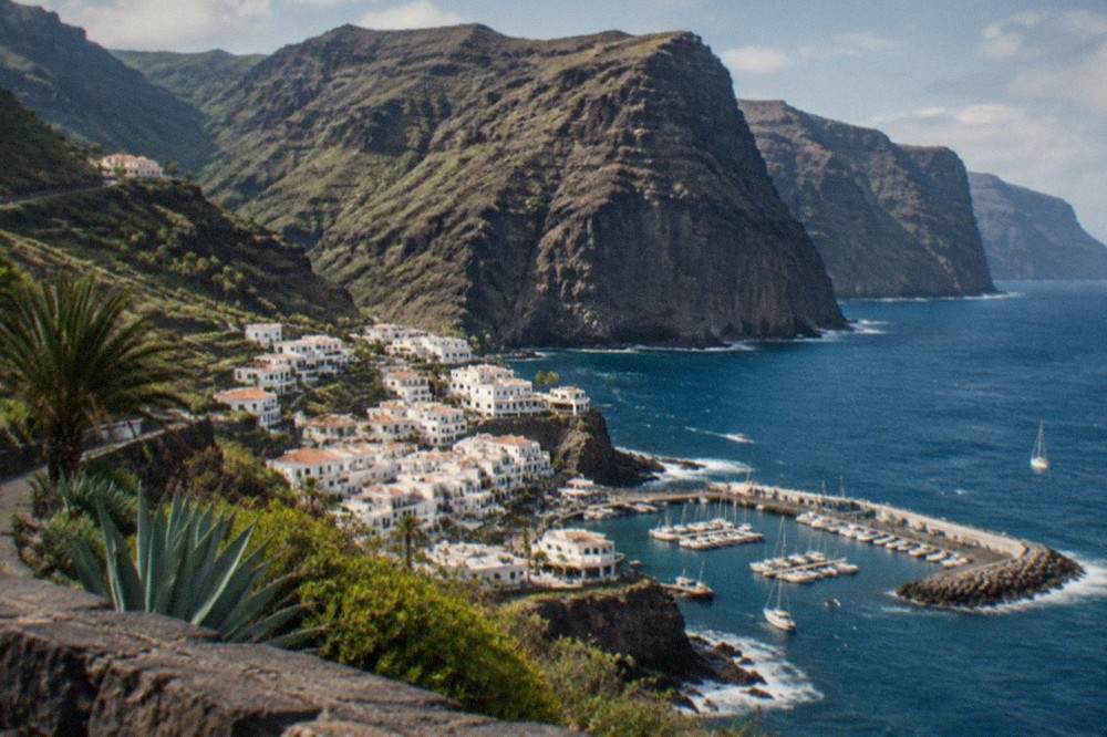 A village of white buildings at the base of enormous cliffs beside a marina