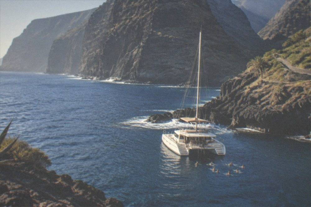 A catamaran moored in a rocky cove with people swimming near the stern