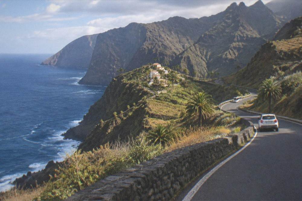 A narrow road winding between dry hills toward cliffs in the distance