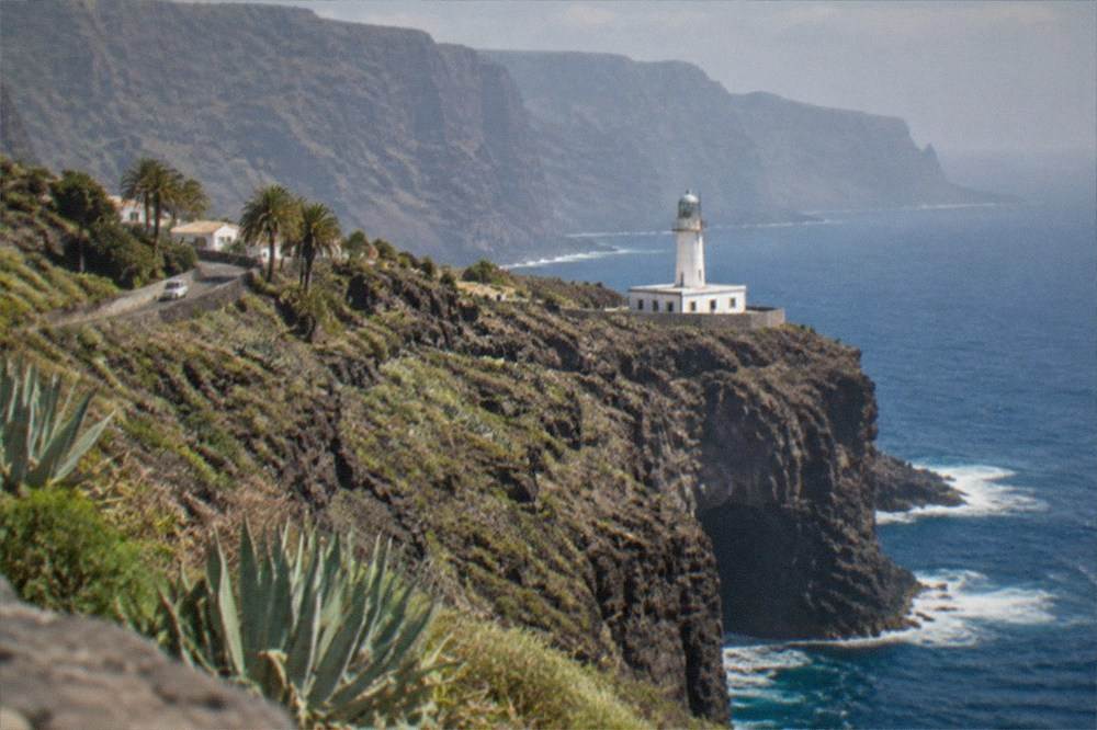 A white lighthouse on a rocky headland with cliffs along the horizon