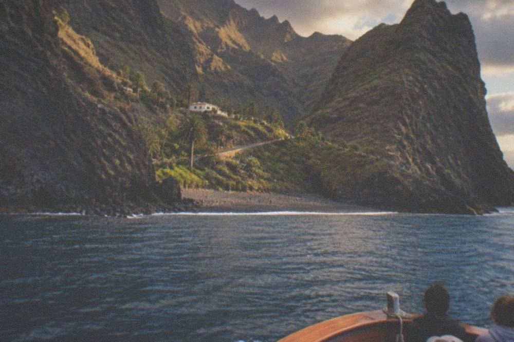 A wooden boat approaching a pebble cove at the foot of tall cliffs in evening light