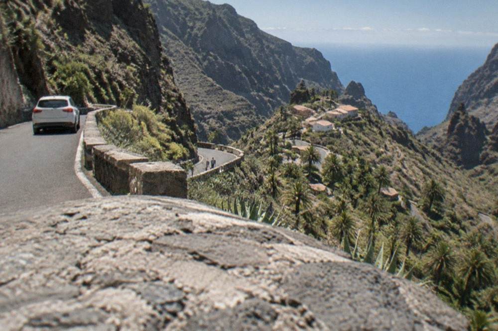 A narrow mountain road winding down a steep hillside towards a clustered village below