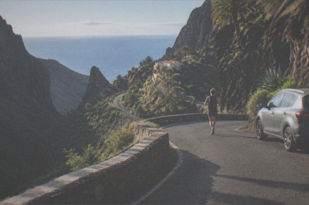 A parked car on a sharp hairpin bend of a narrow mountain road above a ravine