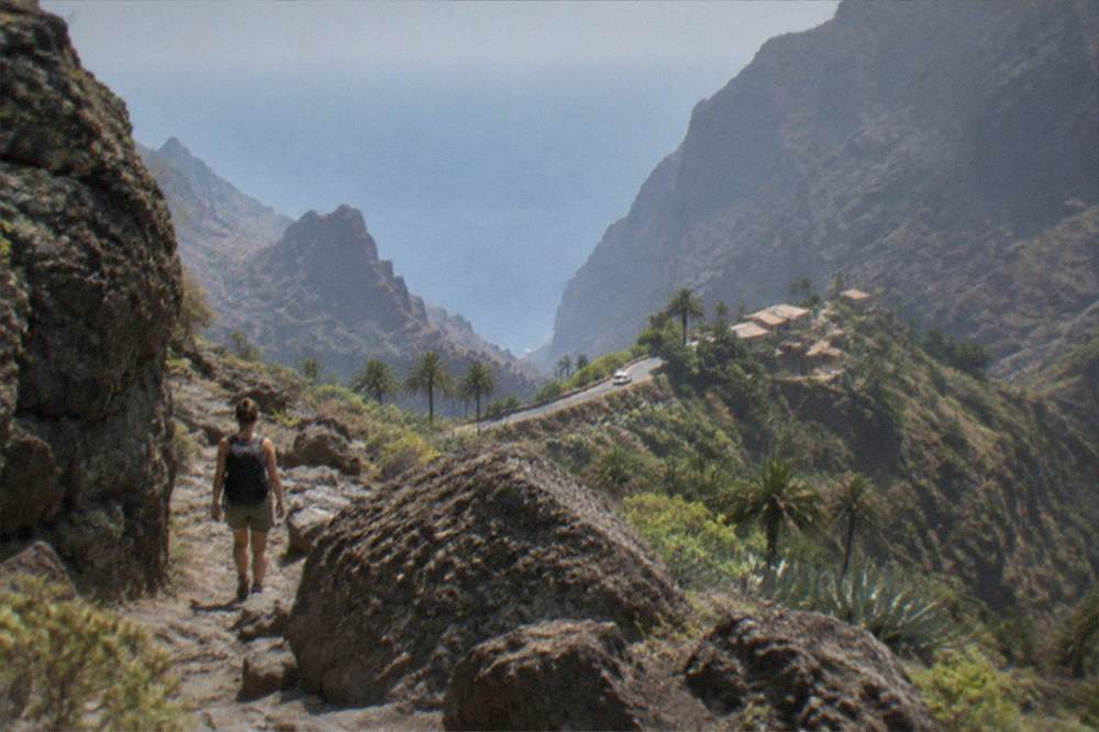 A hiker in boots and a backpack on a stony path between large boulders in a ravine