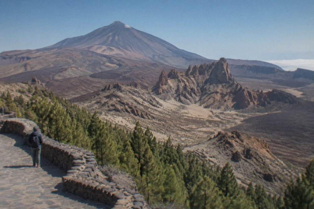 A stone viewpoint platform above pine forest with Mount Teide rising in the distance under a clear sky