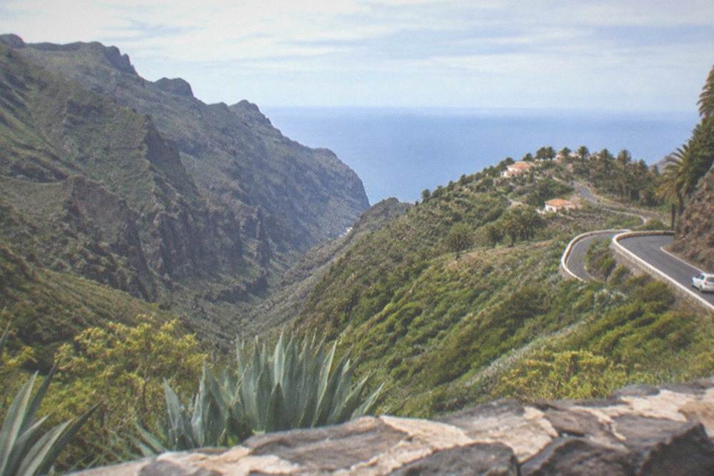 A narrow mountain road winding through green hills with the sea visible far below