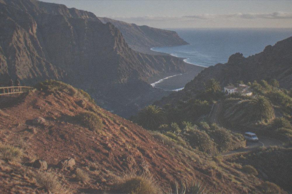 A red-toned hill beside a wide sandy beach with the ocean beyond