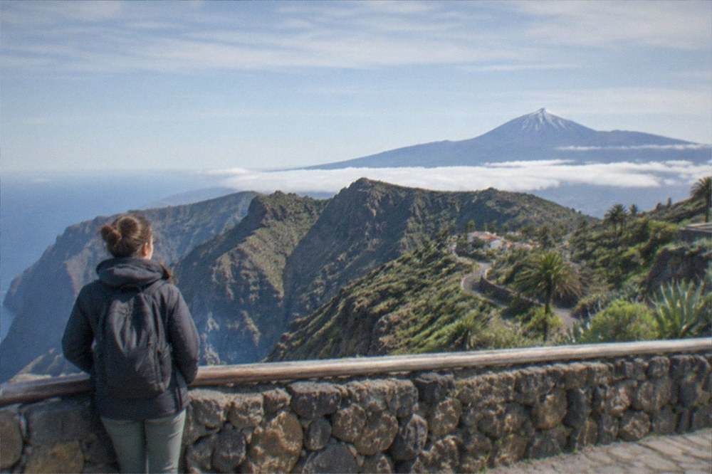 A high mountain viewpoint above a layer of clouds with a snow-dusted volcanic cone in the distance