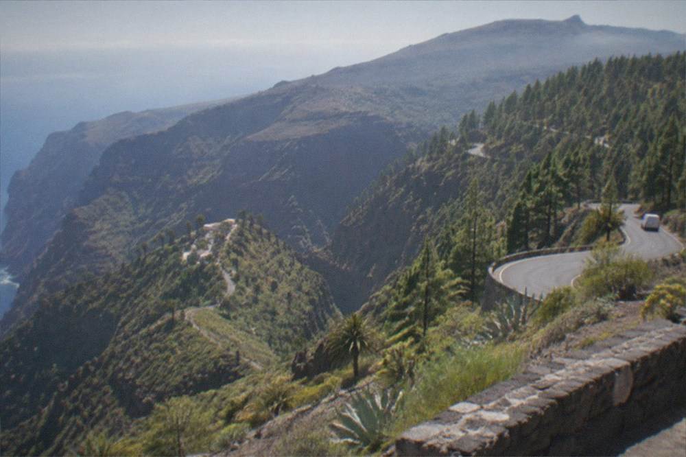 A winding mountain road climbing through pine forest towards a volcanic plateau