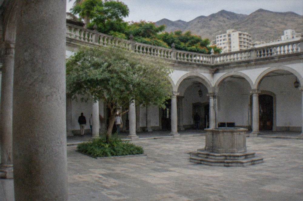 A quiet arcaded courtyard inside a neoclassical former hospital building, plain stone columns around a paved yard